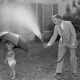 A man spraying a hose at a little kid with an umbrella