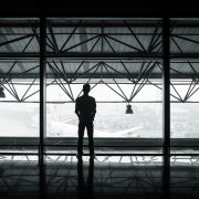 Man standing on an upper floor of an open air building looking out onto a tarmac with an airplane.