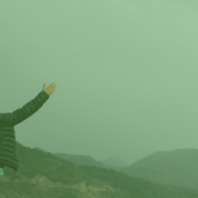image of man standing in front of foggy mountains with arms stretched up to the sky
